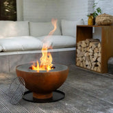 Fire pit with flames in an outdoor setting with a couch and stacked logs.
