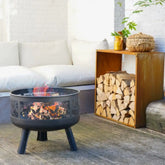 Fire pit with flames in a living room setting with a wooden shelf and firewood.