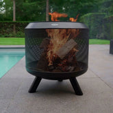 Black mesh fire pit with flames burning outdoors near a pool