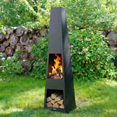 Tall outdoor fireplace with fire burning and logs stacked, set against a natural garden background.