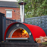 Red outdoor pizza oven with fire inside, placed on a patio area.
