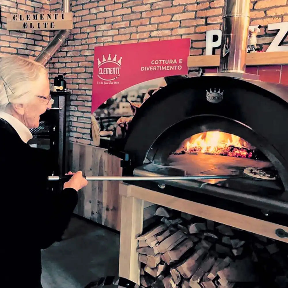 Person using a pizza oven with a brick wall and promotional sign in the background