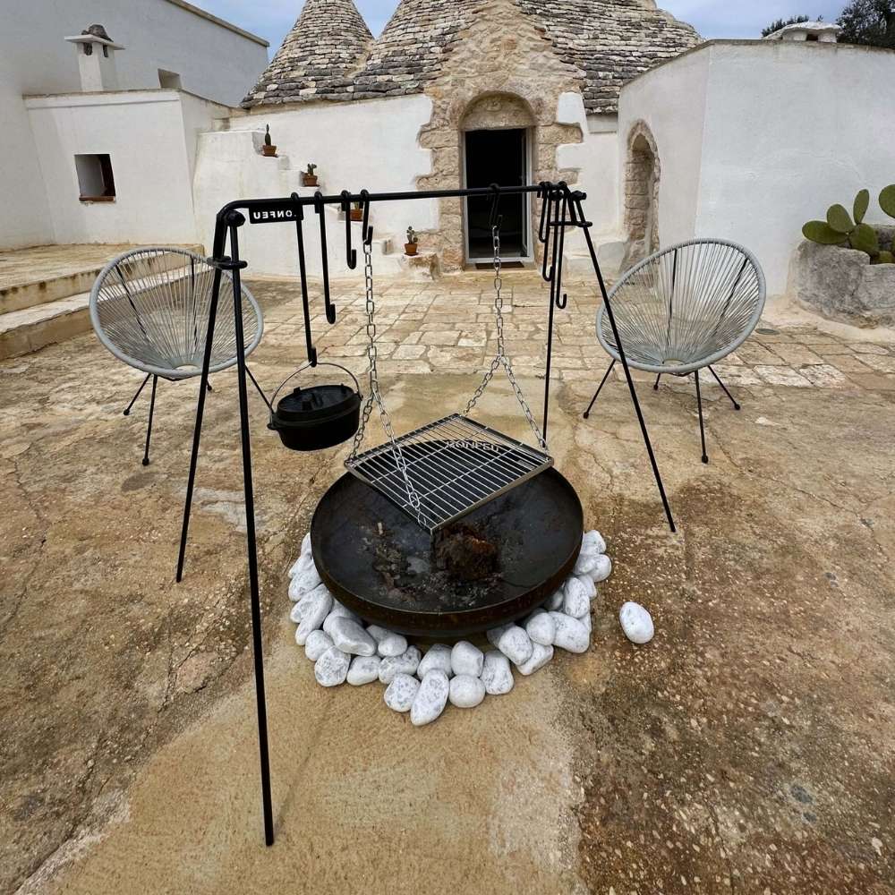 Outdoor setting with a fire pit, chairs, and cooking equipment in front of a traditional building.