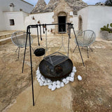 Outdoor setting with a fire pit, chairs, and cooking equipment in front of a traditional building.
