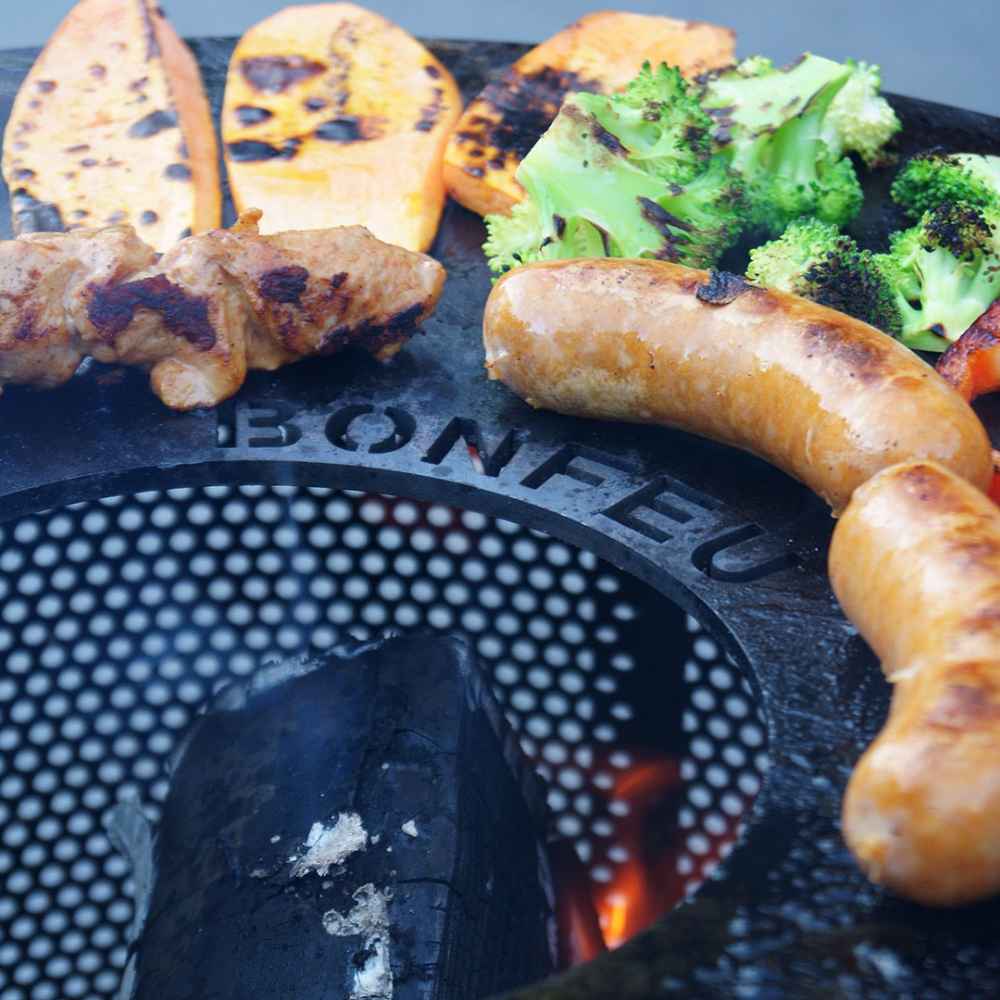 Grilled sausages and vegetables on a grill with 'BONFIRE' branding.