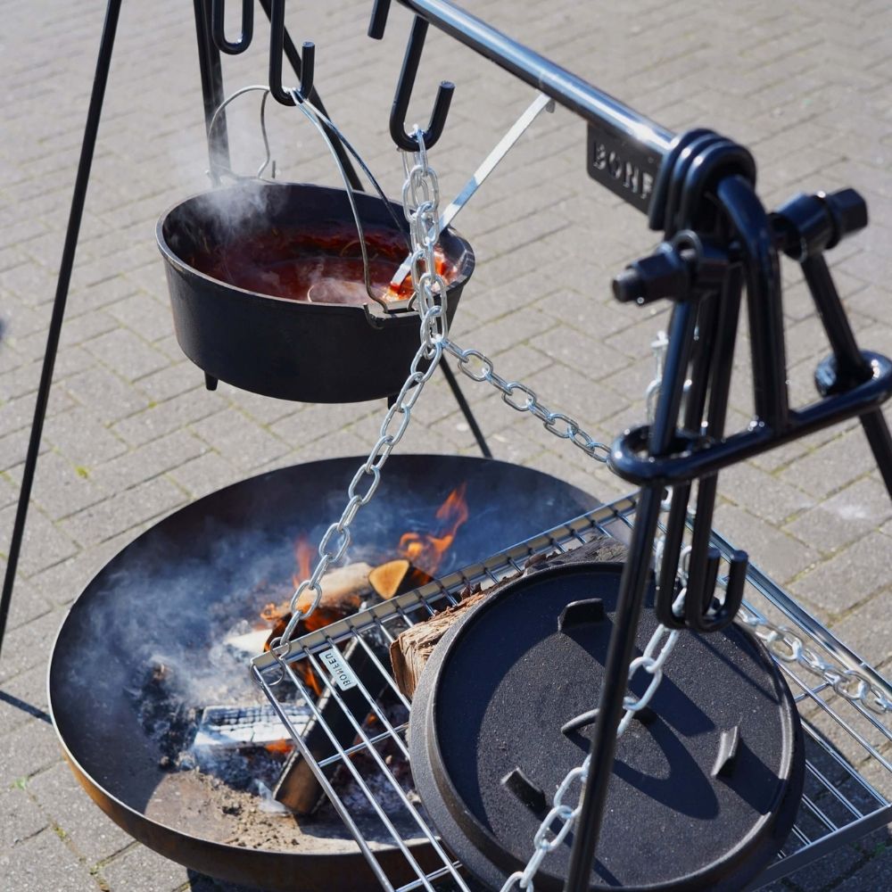 Outdoor cooking setup with a pot over a fire on a metal stand.
