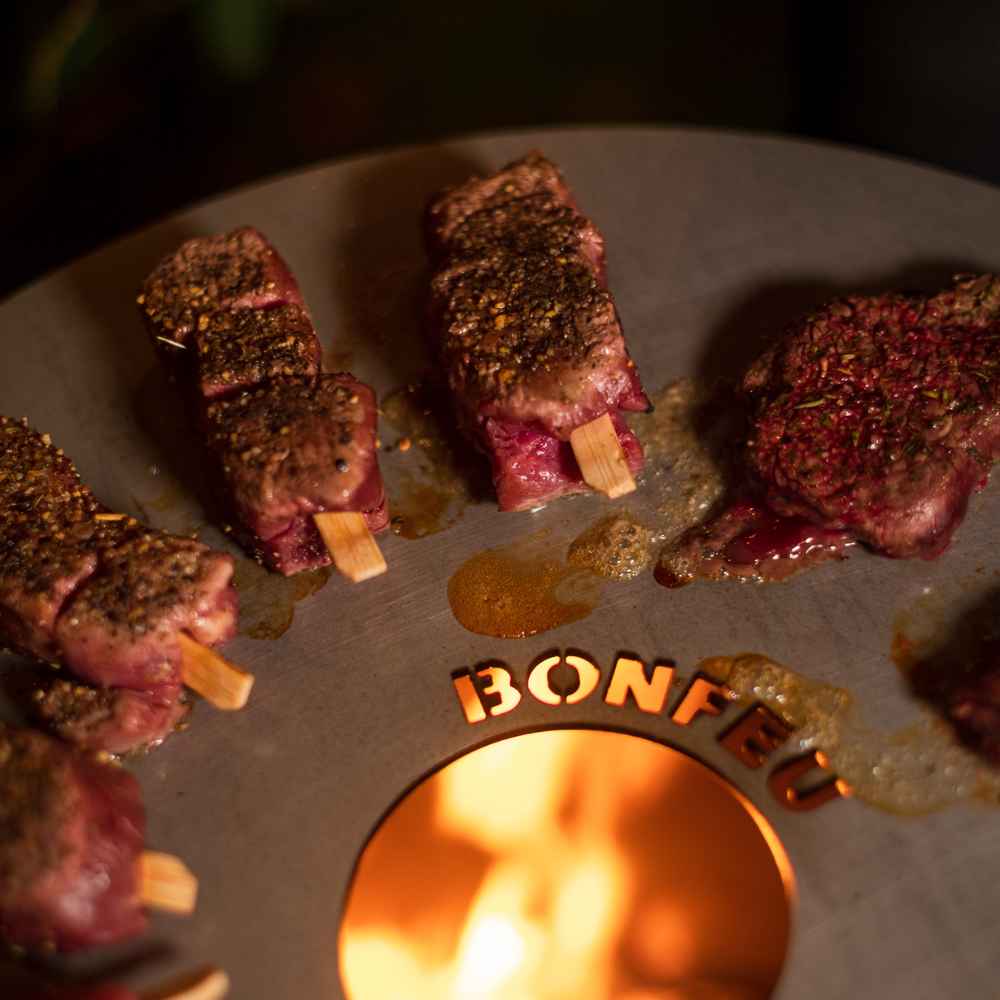 Grilled meat skewers on a grill with 'Bonfire' branding.