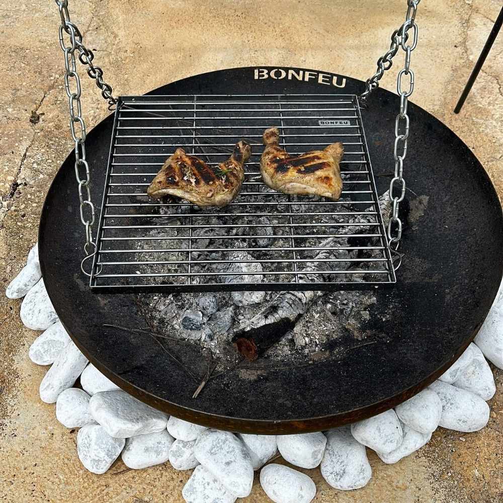 Bonfeu grill over a fire pit with two pieces of meat cooking.