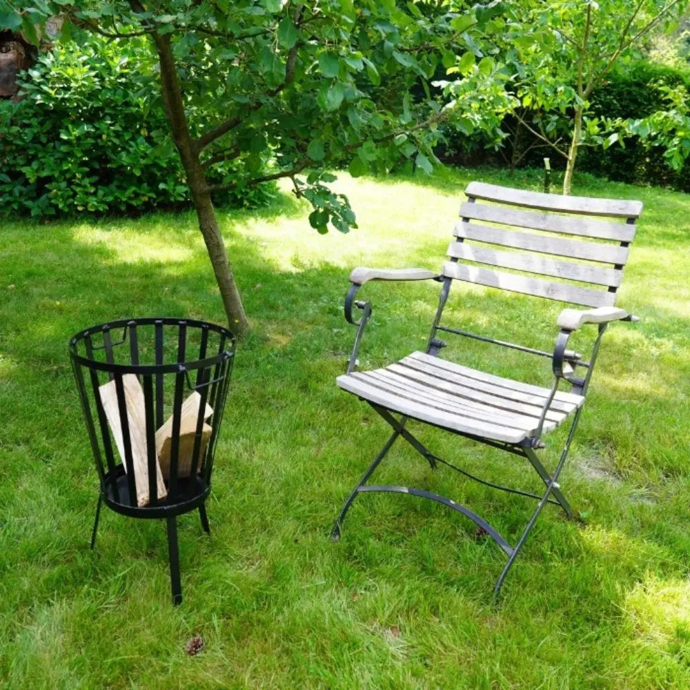Wooden chair and black metal fire basket with firewood on a grassy lawn