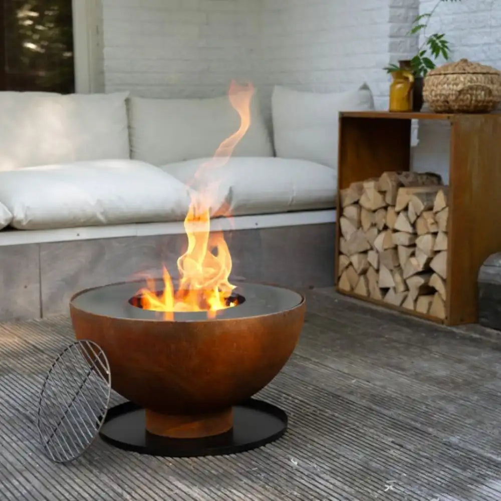 Fire pit with flames in an outdoor setting with a couch and stacked logs.