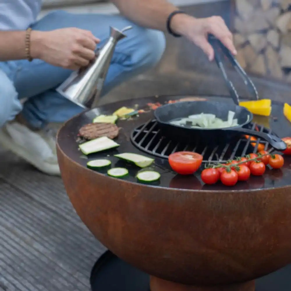 Person grilling vegetables on a fire pit with tongs