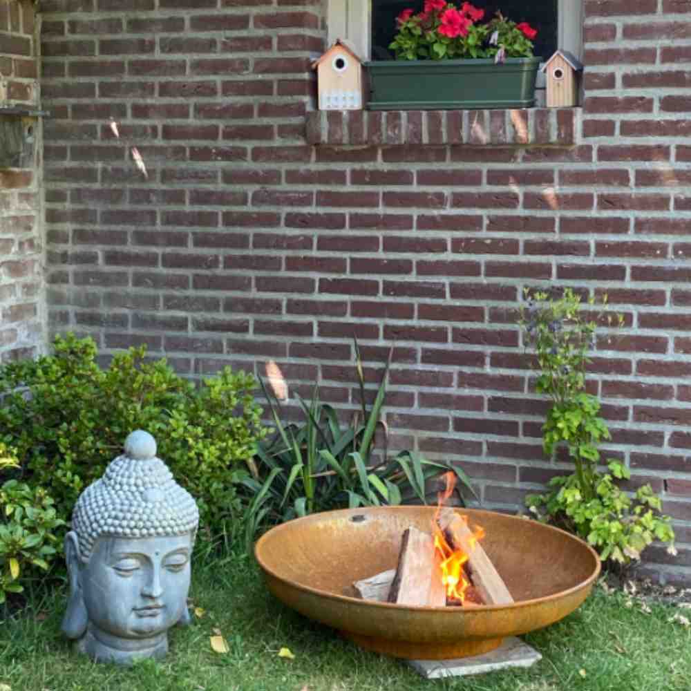 Outdoor setting with a fire pit, Buddha statue, and brick wall with plants.
