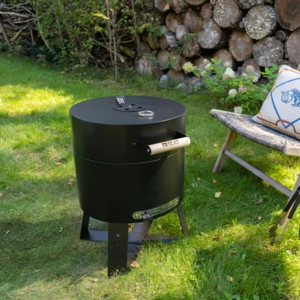 Black barbecue grill on grass with stacked logs in the background