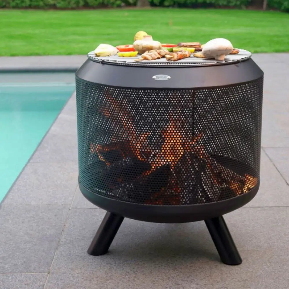 Outdoor fire pit with flames and food on a patio near a pool