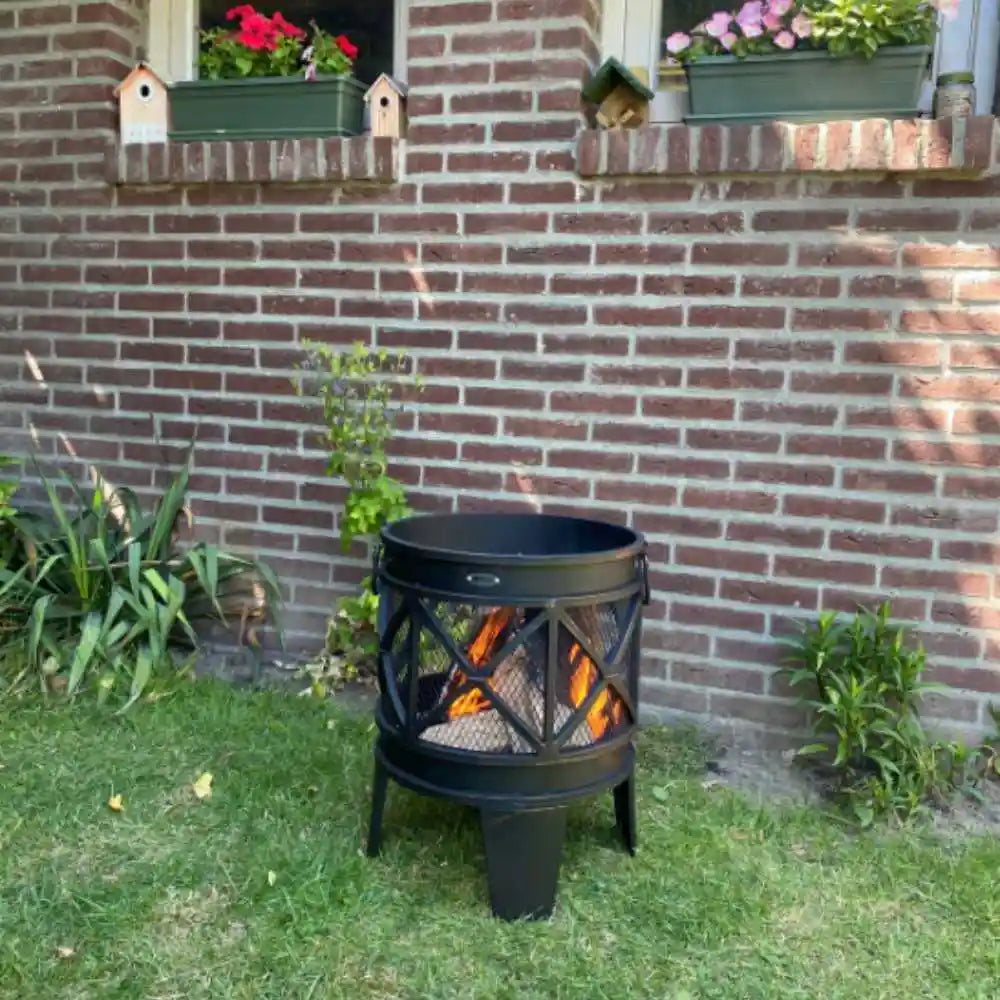 Black outdoor fire pit in a garden with a brick wall and plants in the background