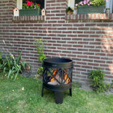 Black outdoor fire pit in a garden with a brick wall and plants in the background