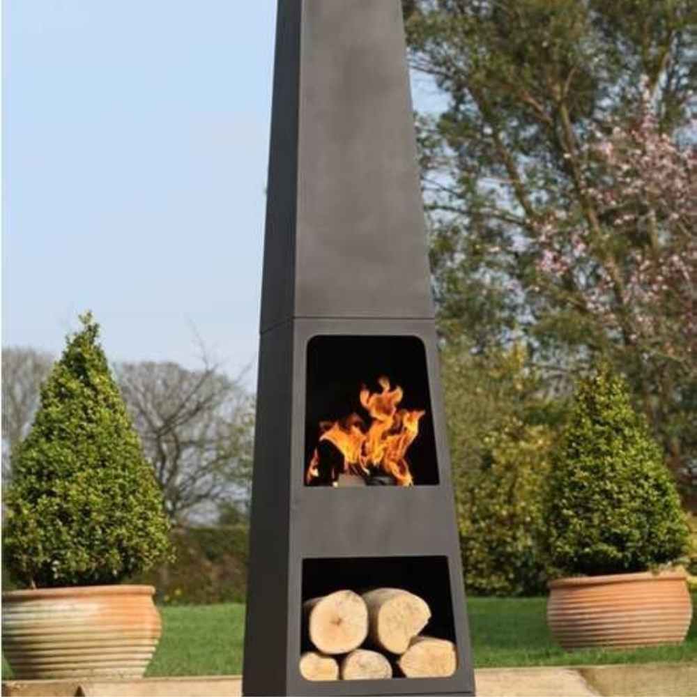 Tall outdoor fireplace with fire burning and logs inside, set against a garden backdrop.