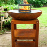 Rust-colored fire pit with flames on a wooden stand in an outdoor setting