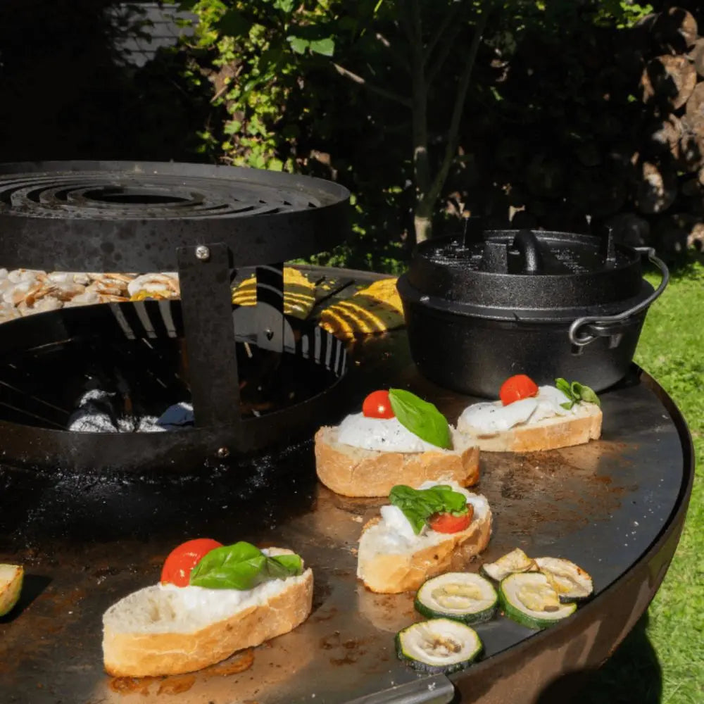 Outdoor cooking setup with bruschetta on a grill and a pot in the background.