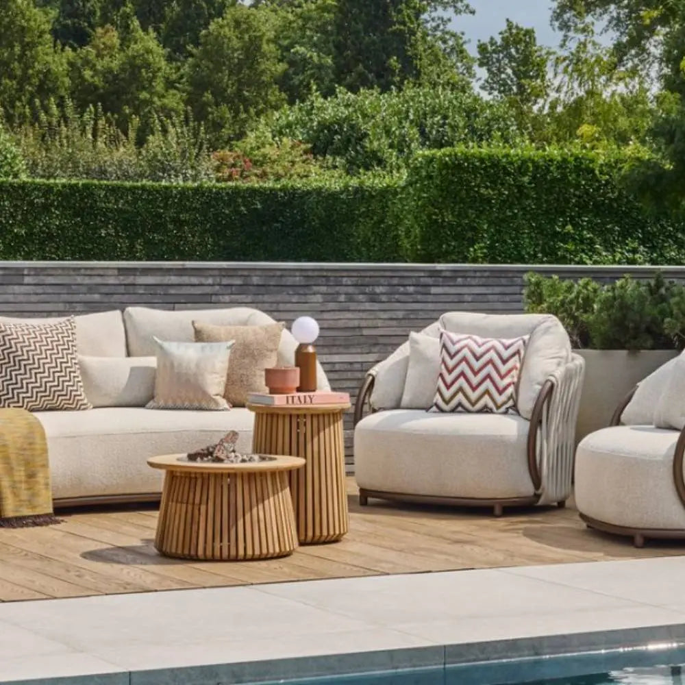 Outdoor patio set with beige furniture, cushions, and a wooden fire pit table by a pool.