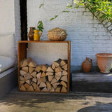 Stack of firewood against a white brick wall with decorative pots and plants.
