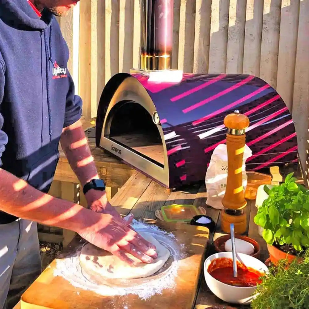 Person making pizza in front of a colorful outdoor pizza oven.