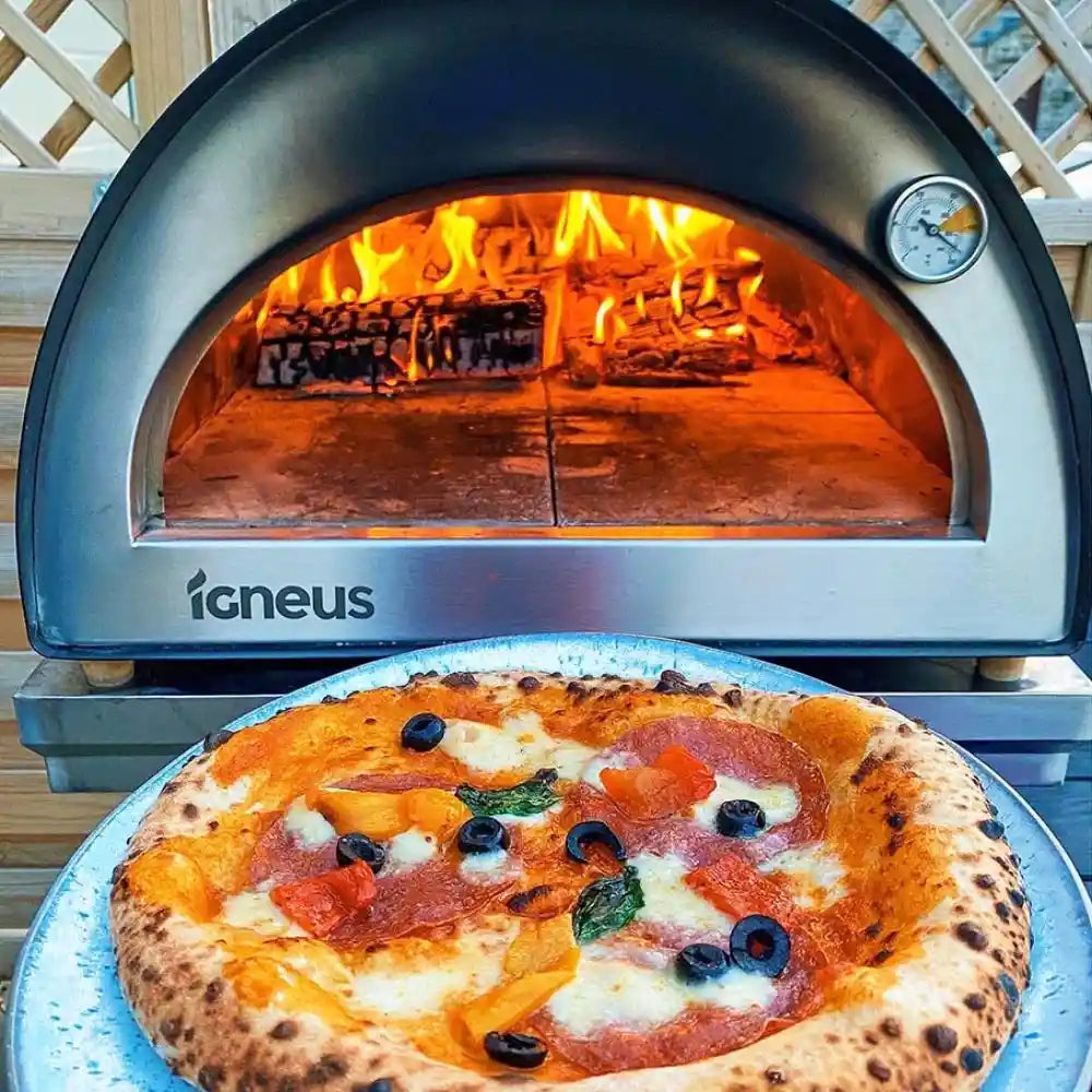 Wood-fired pizza in front of an igneus pizza oven with visible flames.