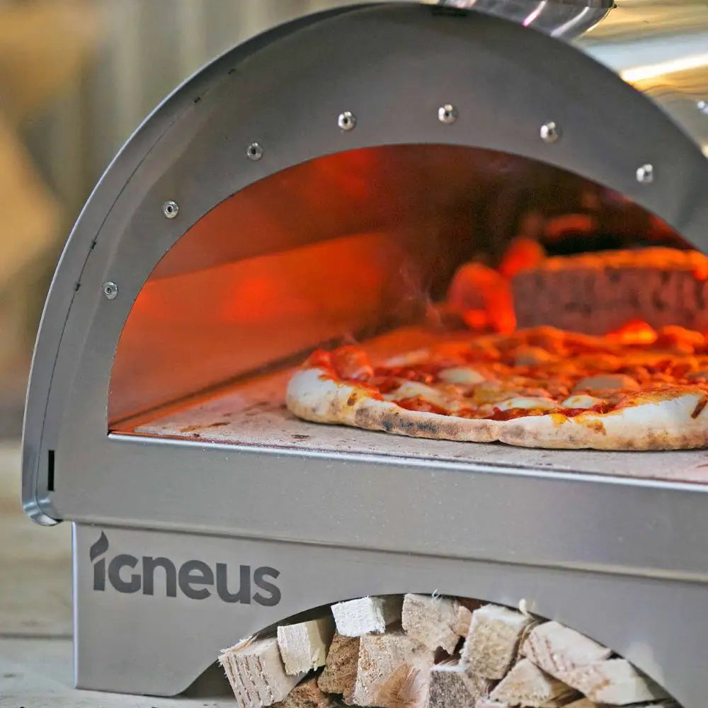 Pizza being cooked in an Igneus pizza oven with wood visible below.