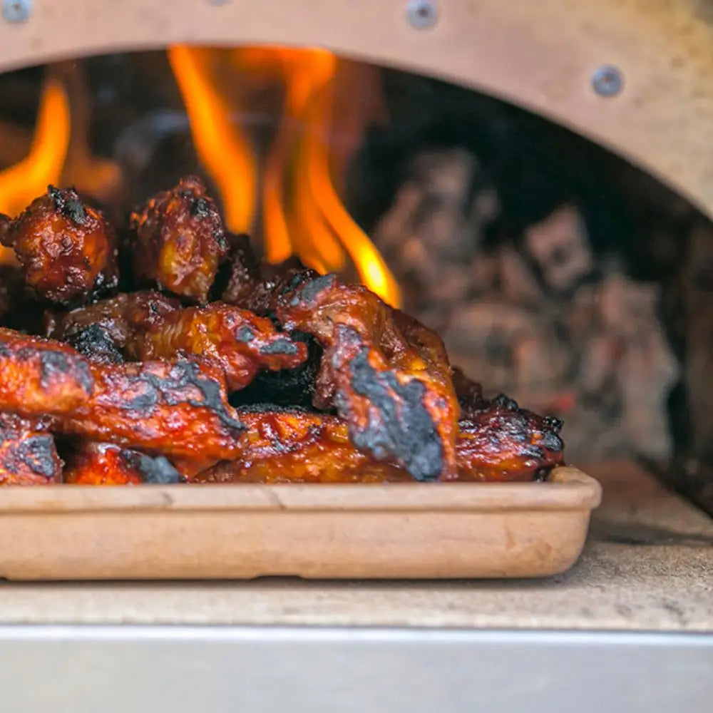 Grilled chicken wings on a wooden board with flames in the background
