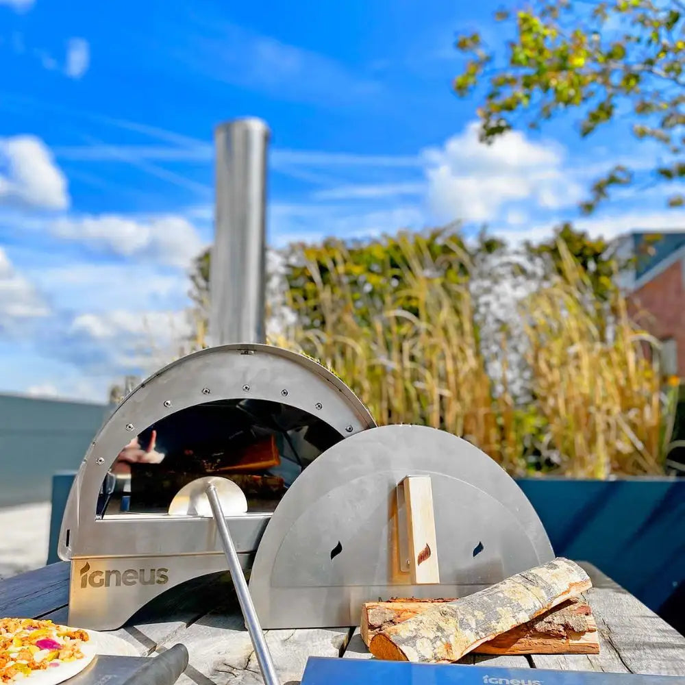 Outdoor pizza oven with a pizza on a wooden table against a blue sky.