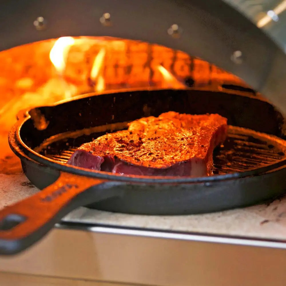 Steak being cooked in a cast iron skillet inside an open oven.