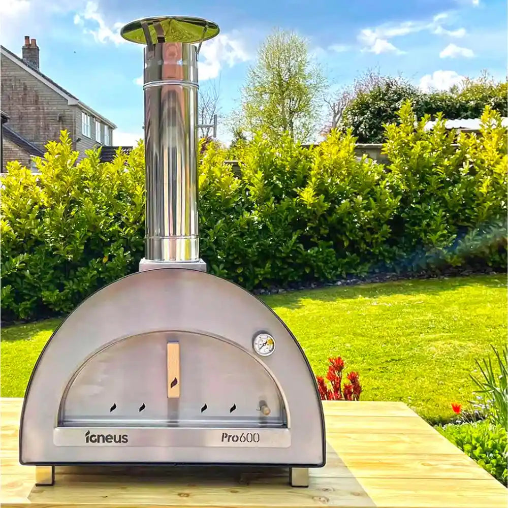 Outdoor pizza oven on a wooden deck with a garden and house in the background