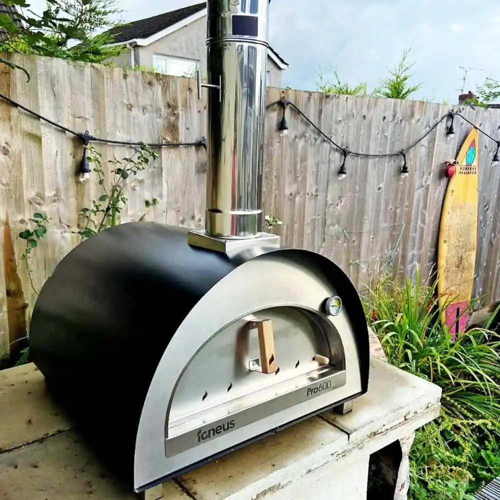 Outdoor pizza oven on a wooden platform with a garden background