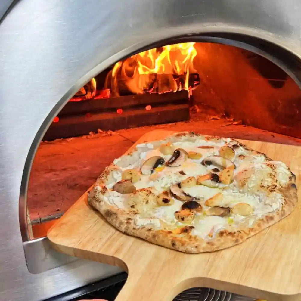 Wood-fired pizza with mushrooms and onions being taken out of a pizza oven.