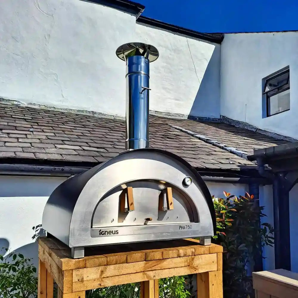 Outdoor pizza oven on a wooden stand with a building in the background