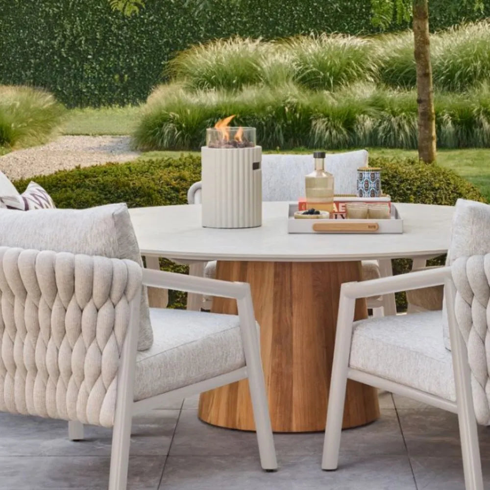 Outdoor patio setting with a round wooden table and beige chairs, featuring a table top burner.