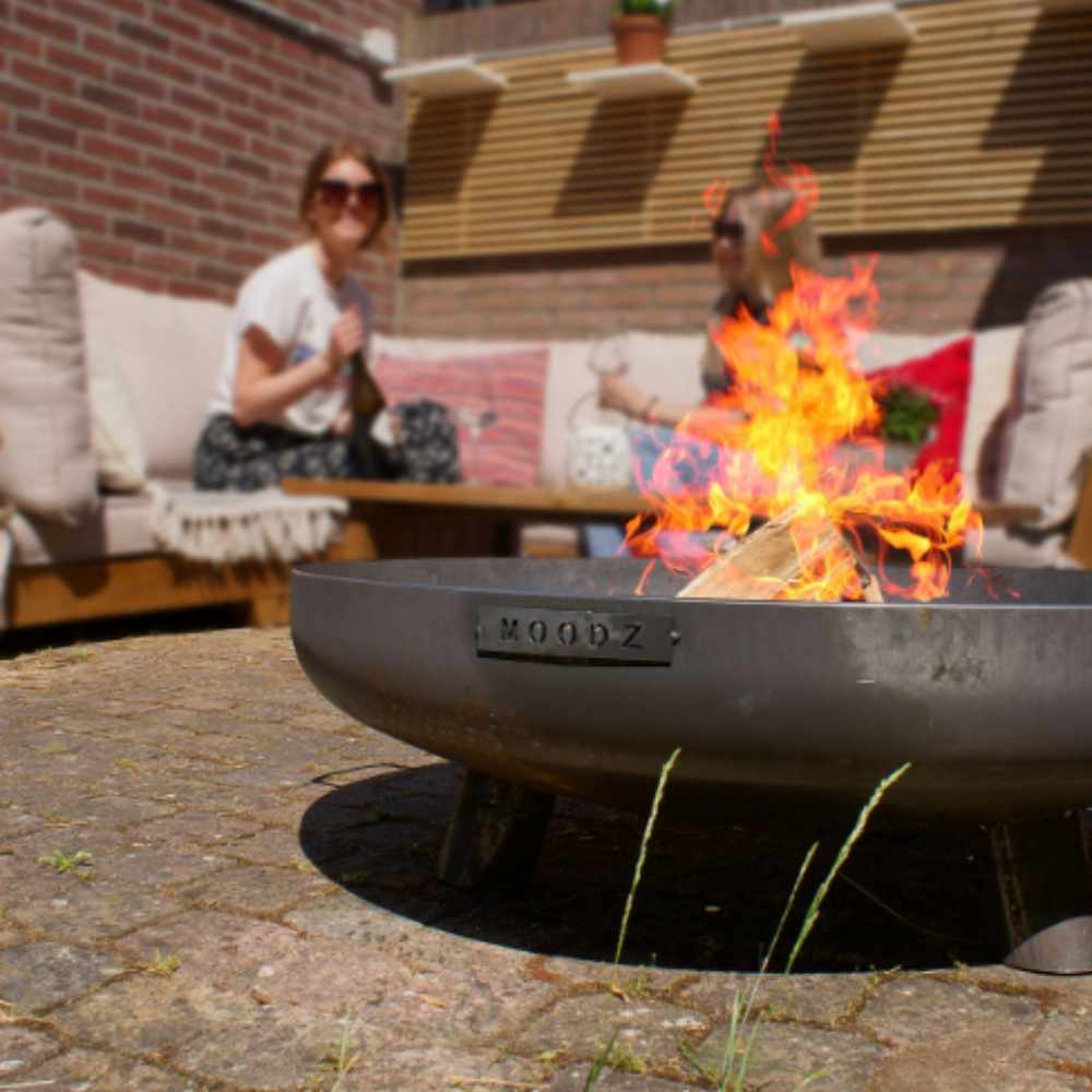 Fire pit with flames on a patio, people sitting in the background