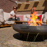 Fire pit with flames on a patio, people sitting in the background
