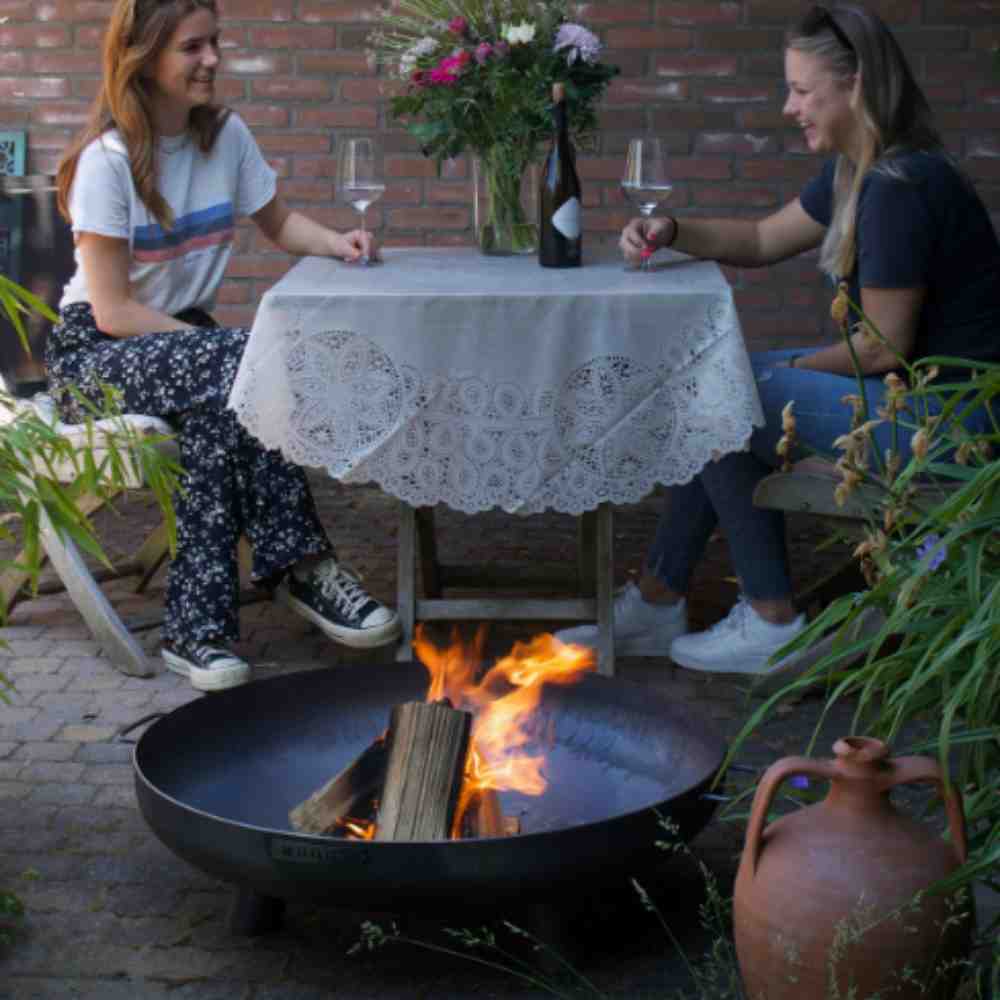 Two people sitting at a table with a fire pit in front of them.