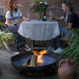Two people sitting at a table with a fire pit in front of them.
