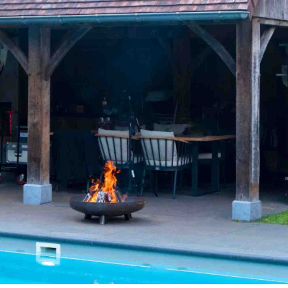 Fire pit by a pool with wooden pergola and chairs in the background