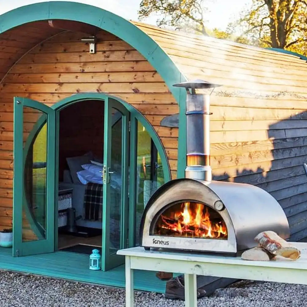 Wood-fired oven in front of a wooden cabin with open doors.