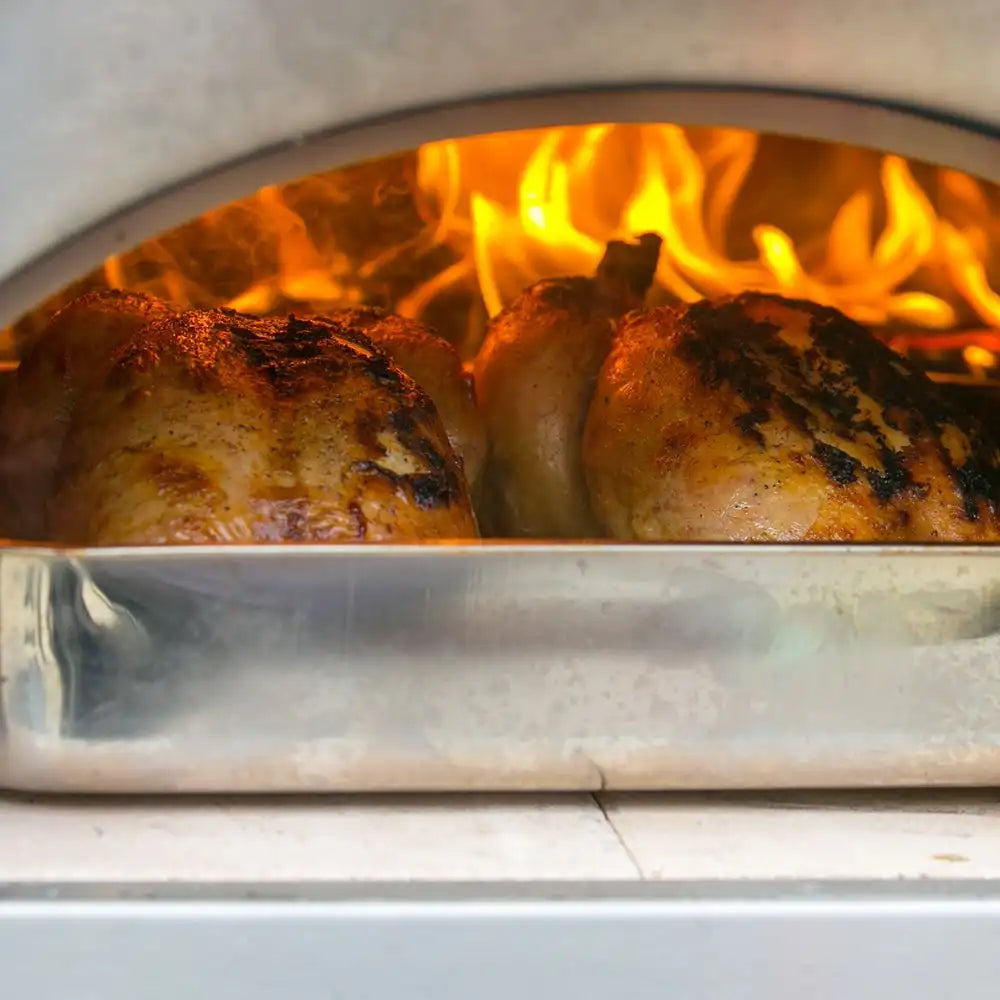 Chicken being cooked inside a wood-fired oven with flames visible.