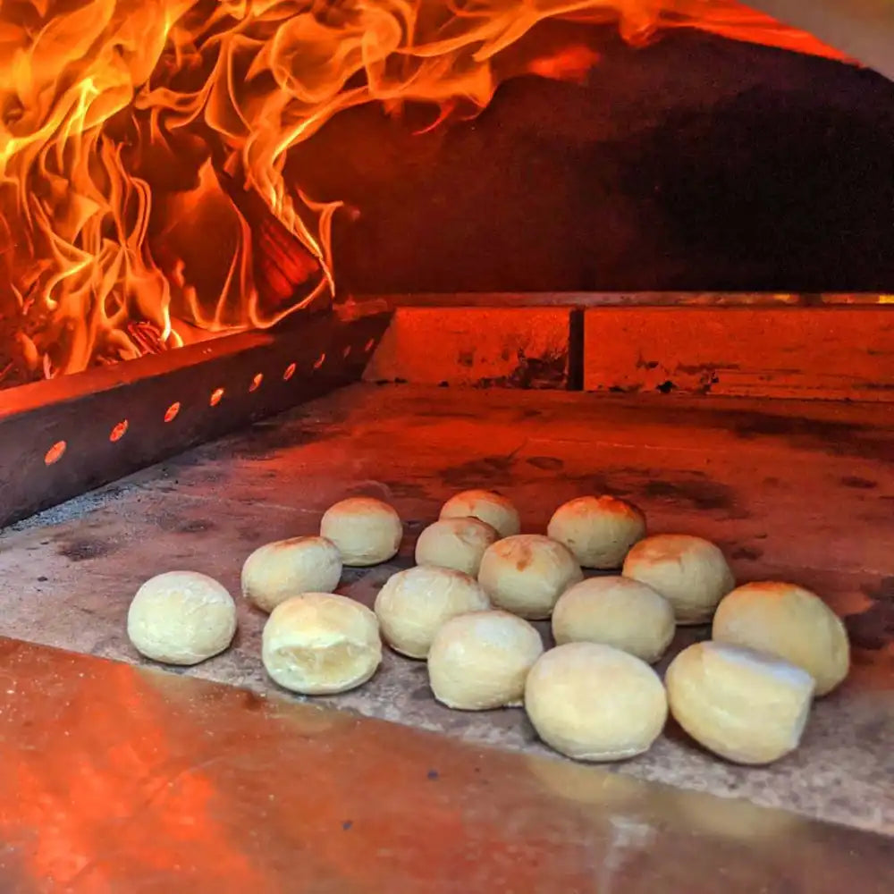 Bread dough balls in a wood-fired oven with flames.