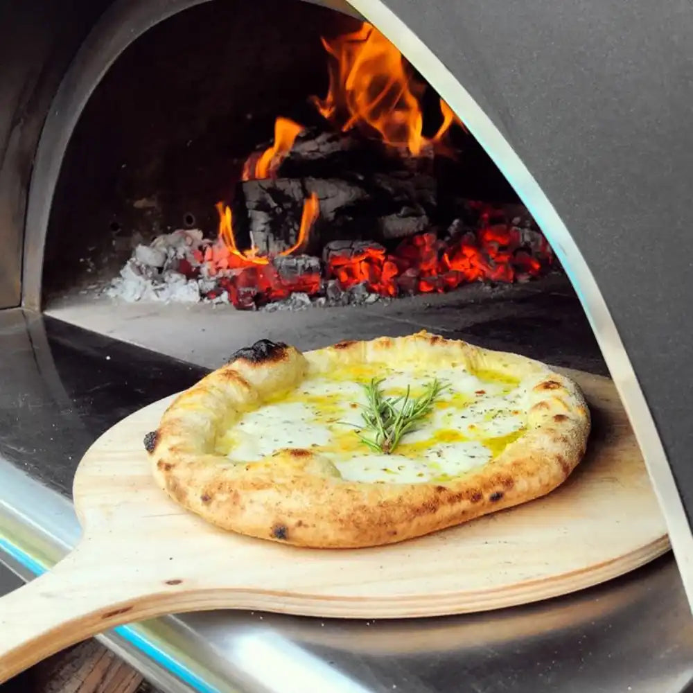 Wood-fired pizza being taken out of a brick oven with flames visible.