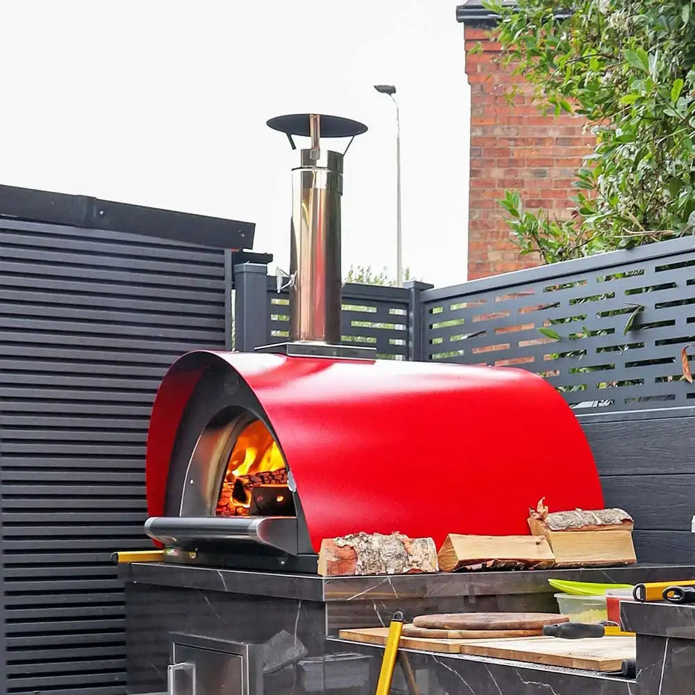 Red outdoor pizza oven with wood inside, set against a modern garden backdrop.