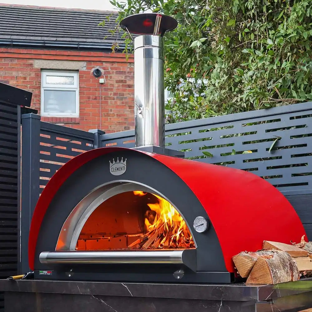Red outdoor pizza oven with fire inside, placed on a patio area.
